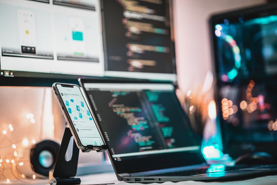 A close-up view of a tech setup with gadgets, coding screen, and smartphone