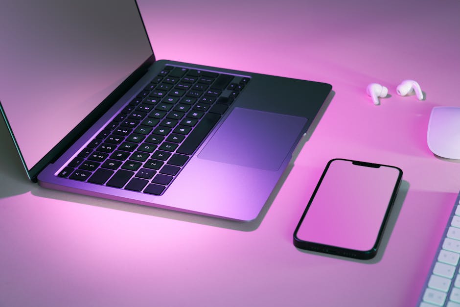 Stylish tech workspace featuring a laptop, smartphone, and earphones under pink lighting