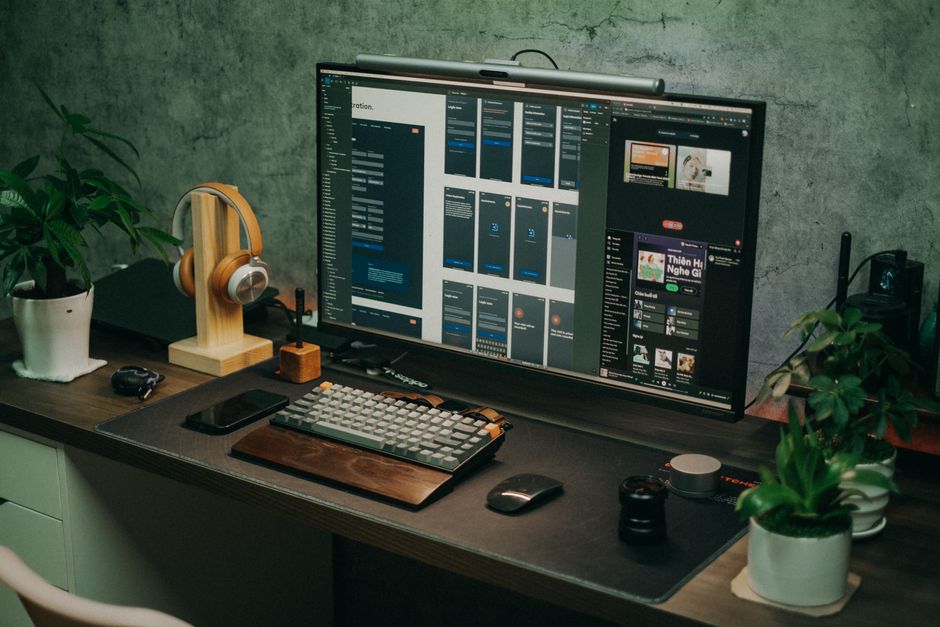 A sleek home office setup featuring a large monitor, keyboard, plants, and headphones