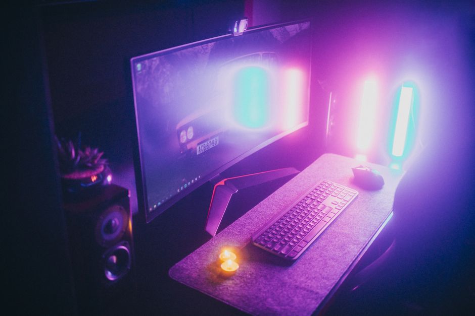 A stylish gaming desk featuring neon lights, keyboard, and monitor in a dark room